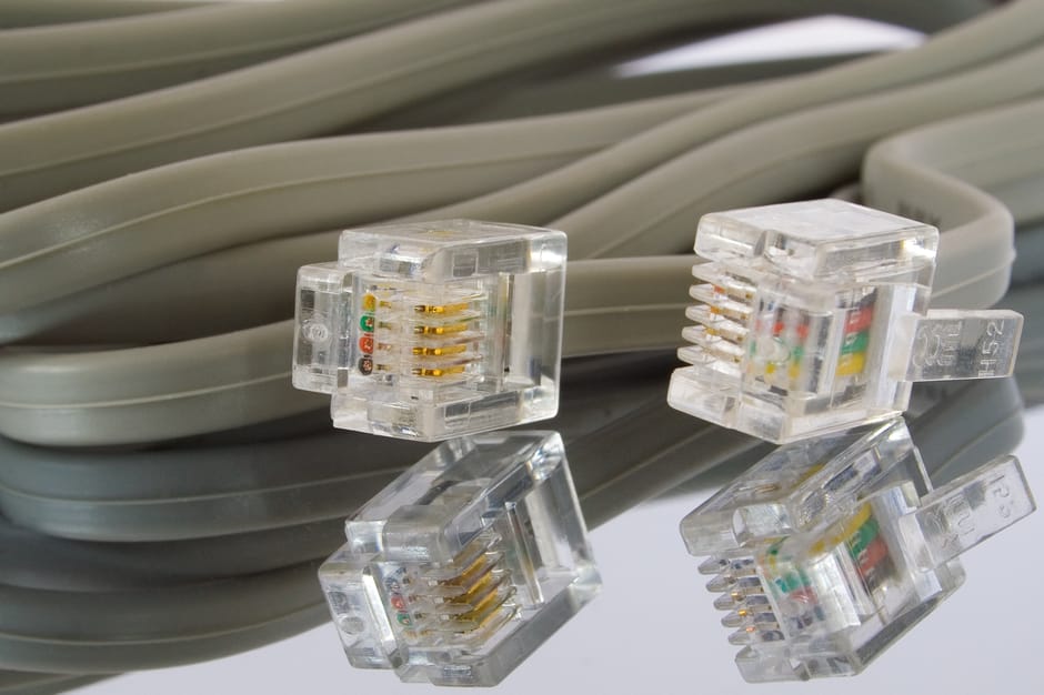 A close-up of a bundle of grey Ethernet cables with a smooth, matte finish, coiled and stacked together, occupying the background. In the foreground, four transparent plastic RJ45 connectors with gold